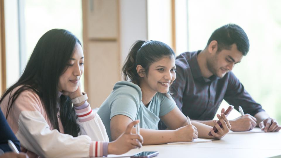 Three students studying together at a desk and smiling.