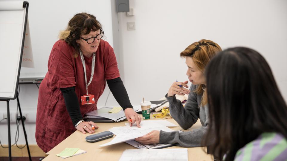 A community learning tutor or lecturer helping a student at a desk.