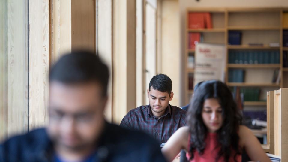 Three students studying and sat down at desks in front of each other in The Callaghan Library.