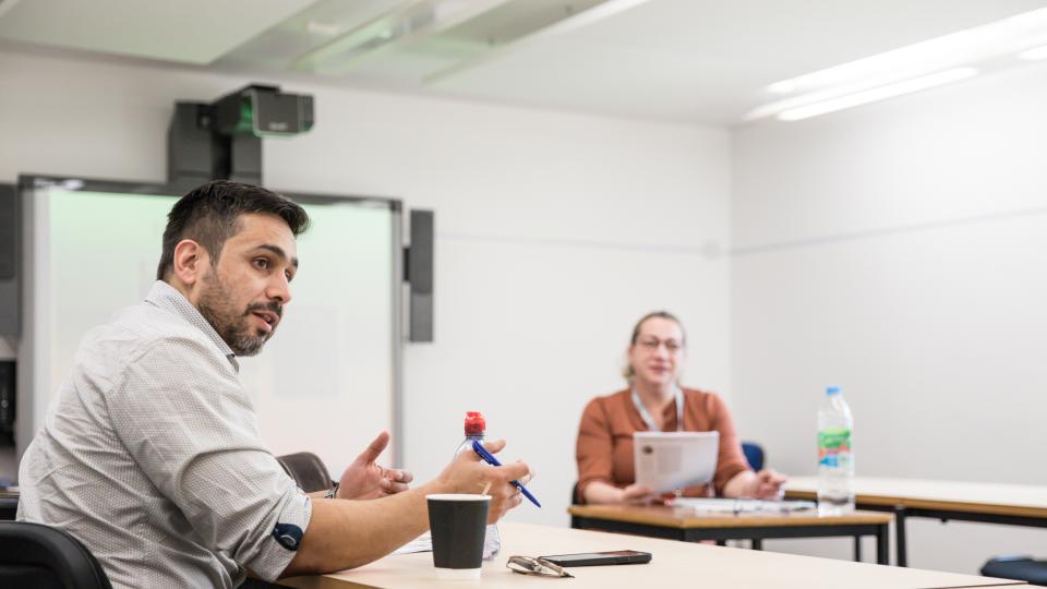 Student seated, discussing work in a classroom setting.