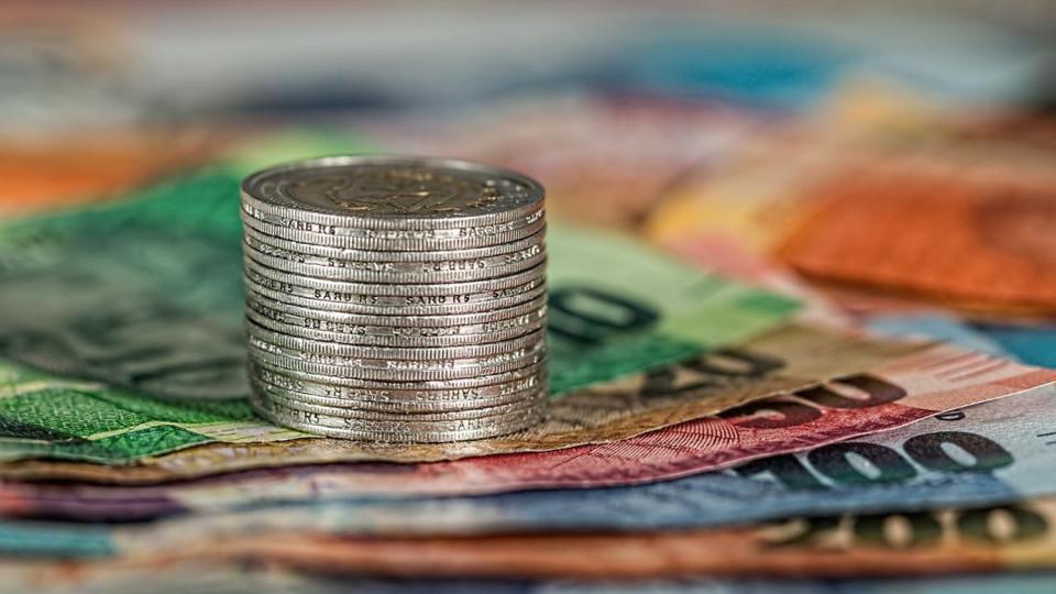 There is a stack of silver round coins on top of an array of different coloured bank notes. The bank notes start at 10 and go up to 200 euros.